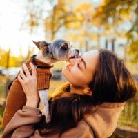 Žena u parku, jesenje boje, mazi se sa kucom, poljubac.