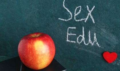 Na tabli piše sex edu, ispred je knjiga na kojoj stoji jabuka.