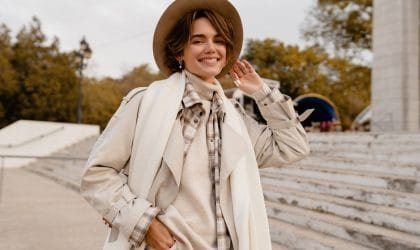 Žena sa bež šeširom, nosi bež rolku, mantil, preko je beli vuneni šal i bež šešir.