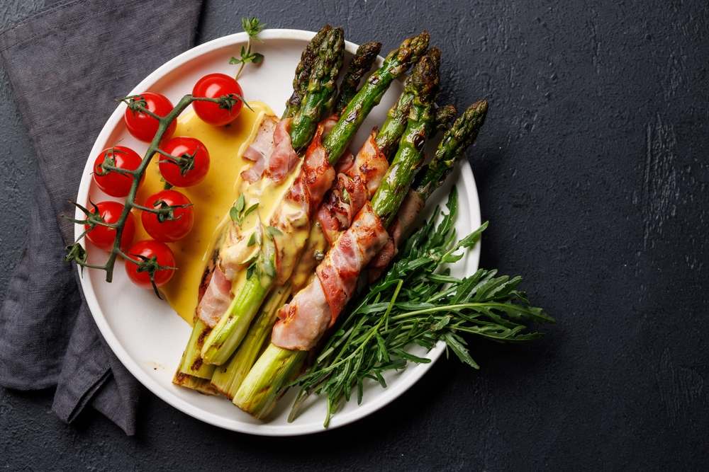 Špargla, asparagus uvijen u slaninu i čeri paradajz na tanjiru.