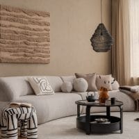 Dnevna soba, bež sofa sa puno jastučića, moderna slika na zidu, neobično zebrasto kanabe, moderni stočić i lampa. Tepih na kome su kućne papuče,