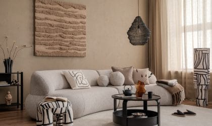 Dnevna soba, bež sofa sa puno jastučića, moderna slika na zidu, neobično zebrasto kanabe, moderni stočić i lampa. Tepih na kome su kućne papuče,