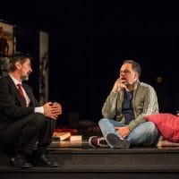 Vojin Ćetković na sceni u crnom odelu, beloj košulji, nosi crvenu kravatu. Predstava "Moje pozorište"