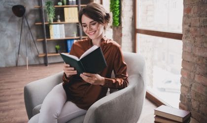 Žena koja sedi u fotelji i sa uživanjem čita knjigu,
