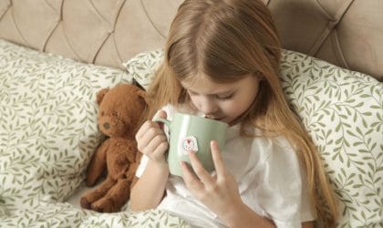 Devojčica u poluležećem položaju, drži medu pored sebe i pije čaj.