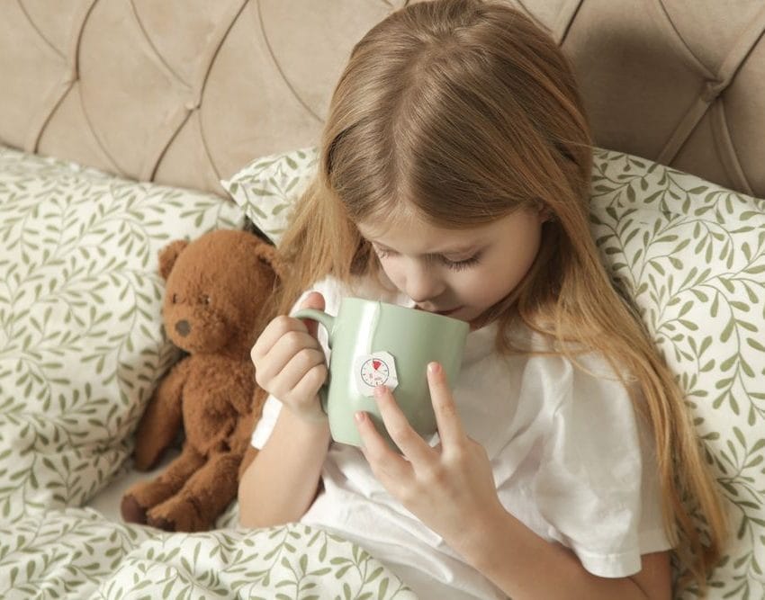 Devojčica u poluležećem položaju, drži medu pored sebe i pije čaj.