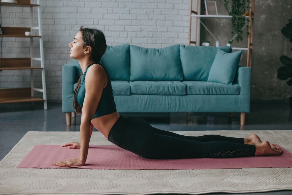 Žena se isteže u dnevnoj sobi, na prostirci.