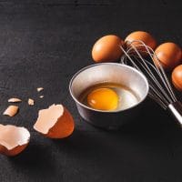 Na stolu su jaja spremna za pripremu. Jedno je razbijeno i u činijici spremno za pripremu.