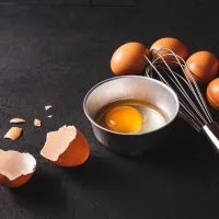 Na stolu su jaja spremna za pripremu. Jedno je razbijeno i u činijici spremno za pripremu.
