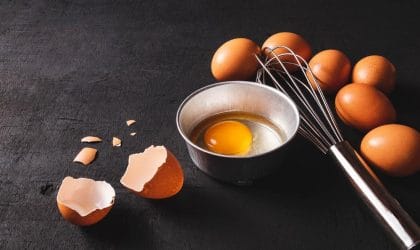 Na stolu su jaja spremna za pripremu. Jedno je razbijeno i u činijici spremno za pripremu.