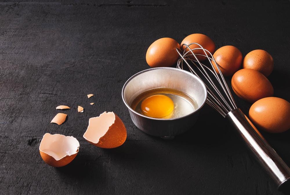 Na stolu su jaja spremna za pripremu. Jedno je razbijeno i u činijici spremno za pripremu.