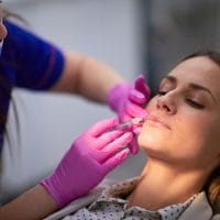 Žena u ordinaciji, doktor primenjuje hijaluron u donji deo lica. Tretira marionetske bore.