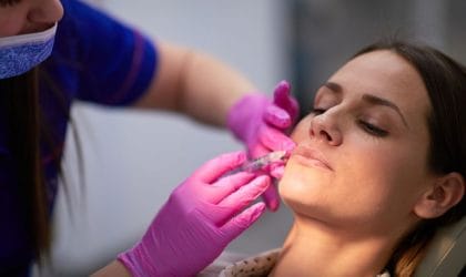 Žena u ordinaciji, doktor primenjuje hijaluron u donji deo lica. Tretira marionetske bore.