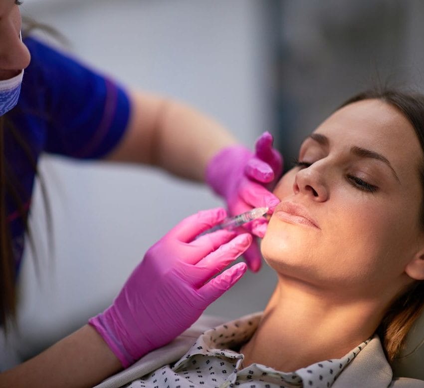 Žena u ordinaciji, doktor primenjuje hijaluron u donji deo lica. Tretira marionetske bore.