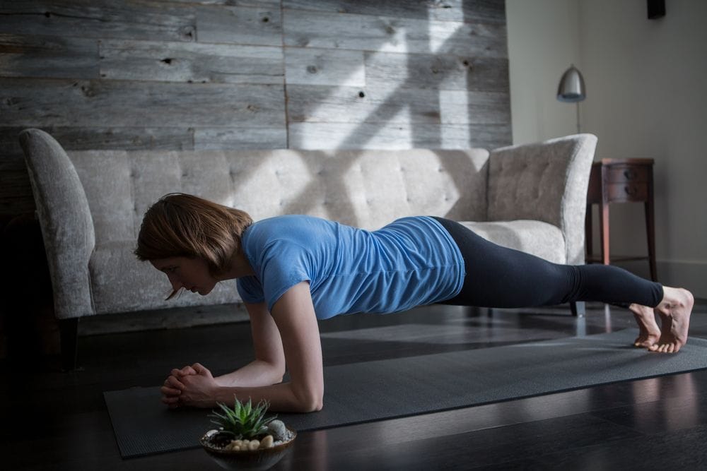 Žena radi plank vežbu u dnevnoj sobi na prostirci.