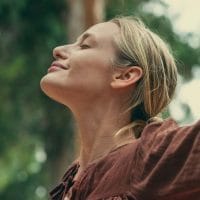 Žena u prirodi, raširila je ruke, opuštena je i udiše svež vazduh.