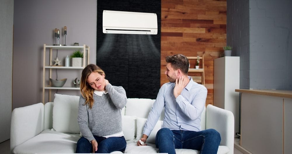 Par sedi na sofi u dnevnoj sobi. Iza njih je klima uređaj. Žena se drži za vrat i ima bolnu grimasu na licu, mu&scaron;karac isto, okrenuo se i gleda u klima uređaj