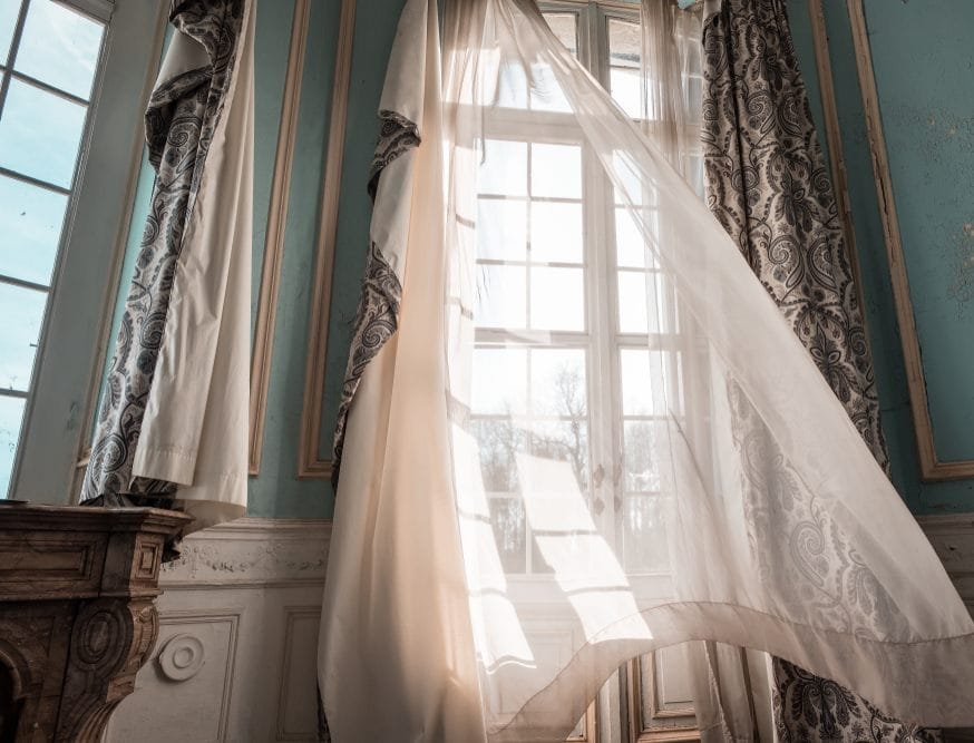 Otvoren prozor u sobi, zavesa leluja na vetru.