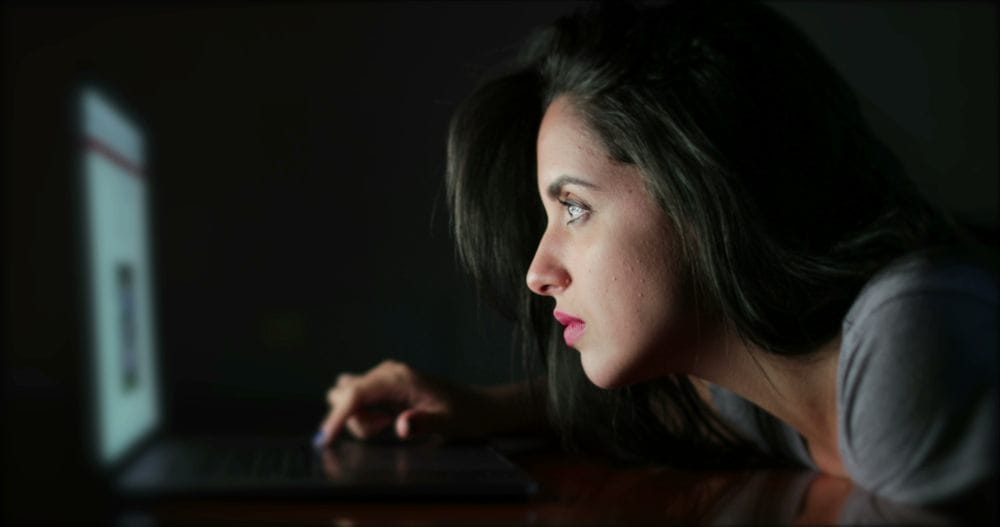 Žena u mraku gleda u ekran laptop-a. Svetlo laptop-a joj osvetljava lice.