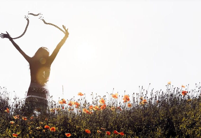 Žena u polju, vidi sa leđa. Simbolično drži ruke u vazduhu i kida stege, lanac koji drži između ruku.