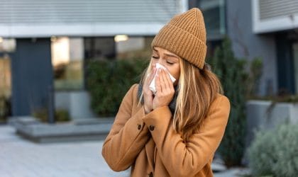 Žena u kaputu, nosi kapu i briše nos maramicom.