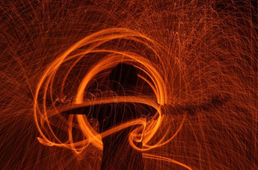 Imaginativna prezentacija. Čovek u krugovima vatre. Figura je tamna, a sve okolo je u jarkim narandžastim tonovima.
