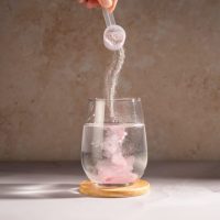 Kašičica sa prahom koji se presipa u čašu sa vodom.