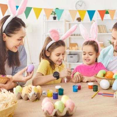 Porodica na okupu. Sede za stolom i ukrašavaju jaja za Uskrs.