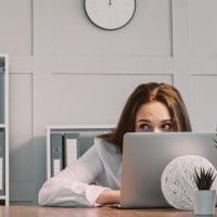 Zaposlena se krije u kancelariji iza lap-top-a i proviruje.