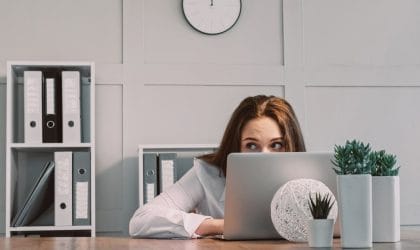 Zaposlena se krije u kancelariji iza lap-top-a i proviruje.
