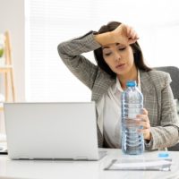 Žena u kancelariji, zamor, umorna je, pored nje na stolu je flaša sa vodom.