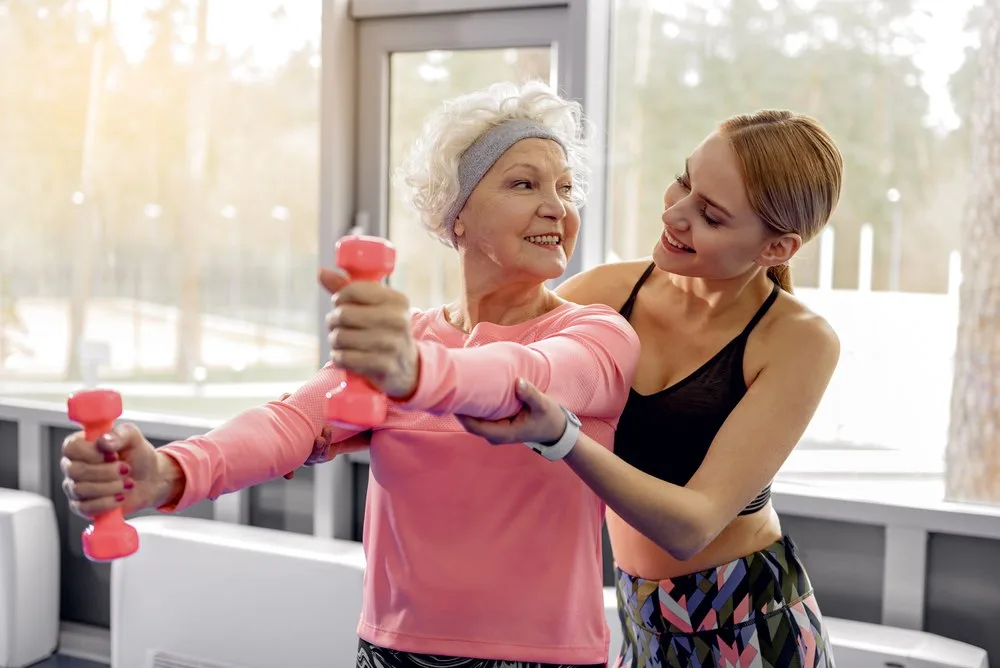 Žena srednjih godina pokazuje svojoj baki kako se vježba s bučicama.
