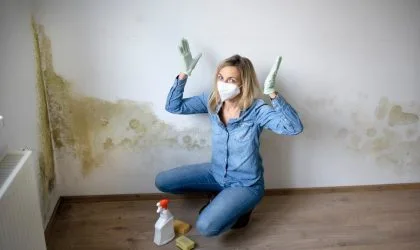 Žena sa maskom na licu, podigla je ruke u vazduh i sprema se da tretira buđ koja se pojavila na zidu u sobi...