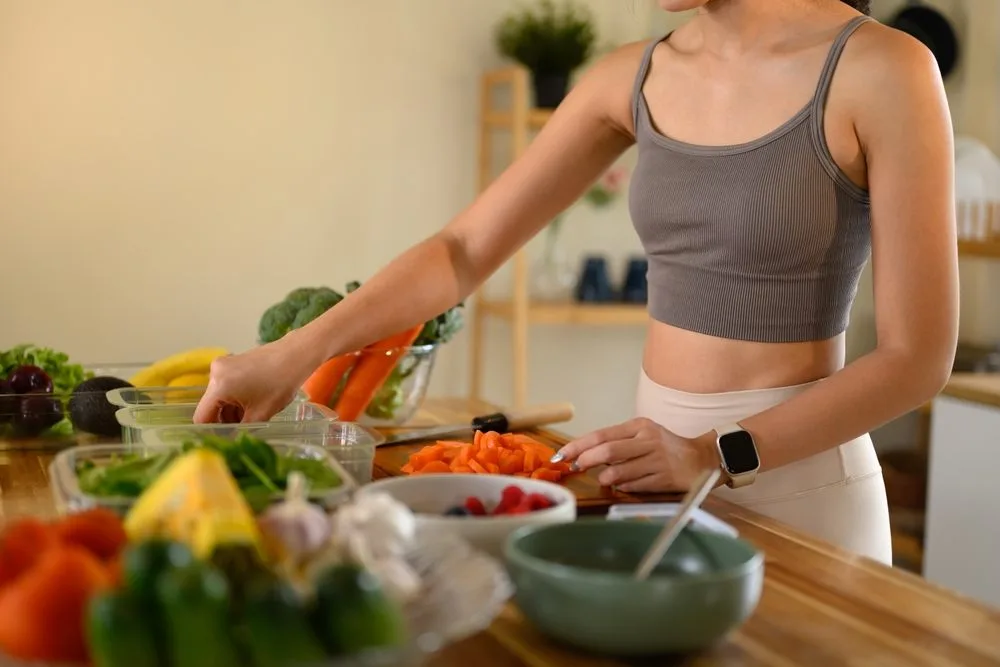 Mr&scaron;ava žena u sportskoj opremi, priprema hranu, na stolu je uglavnom sirovo povrće.