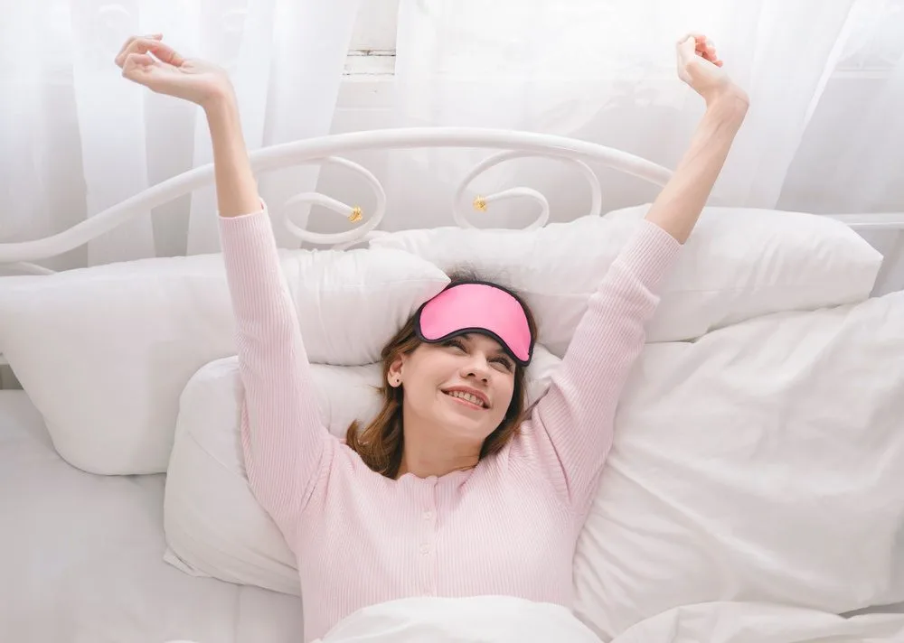 Žena se rasteže u krevetu nakon očigledno dobrog sna.