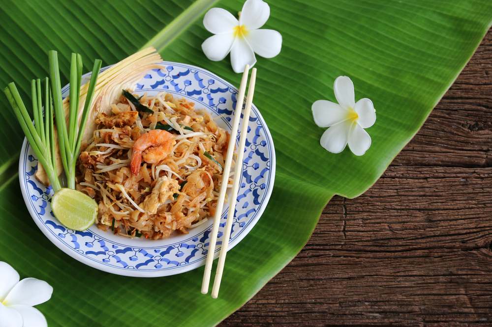 Pad-thai nudle u tanjiru koji stoji na listu bananae. U pozadini su gfrangipani cvetovi.