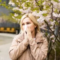 Žena pored drveta u cvatu, drži maramicu na nosu, kija.