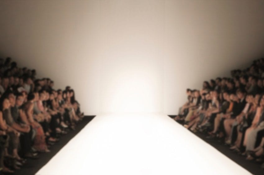 Modna revija, publika je sa obe strane,čeka početak. Pista je dobro osvetljena.