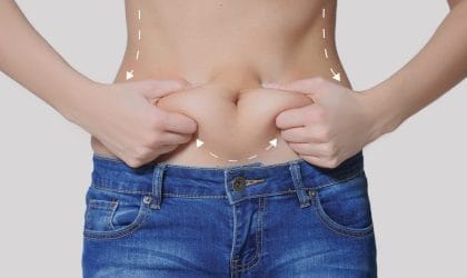 Žena u farmerkama, gornji deo tela je go, rukama drži salo koje se formiralo na stomaku.