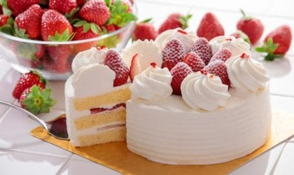 Torta sa jagodama, ukrašena šlagom. Jedno parče je izvađeno i vidi se presek torte, kore, fil i jagode.