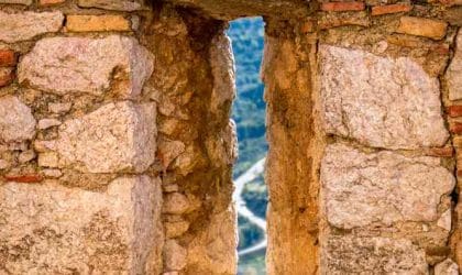 Mali prozor u zidu tvrđave, kroz koji se nazire krivudavi put.