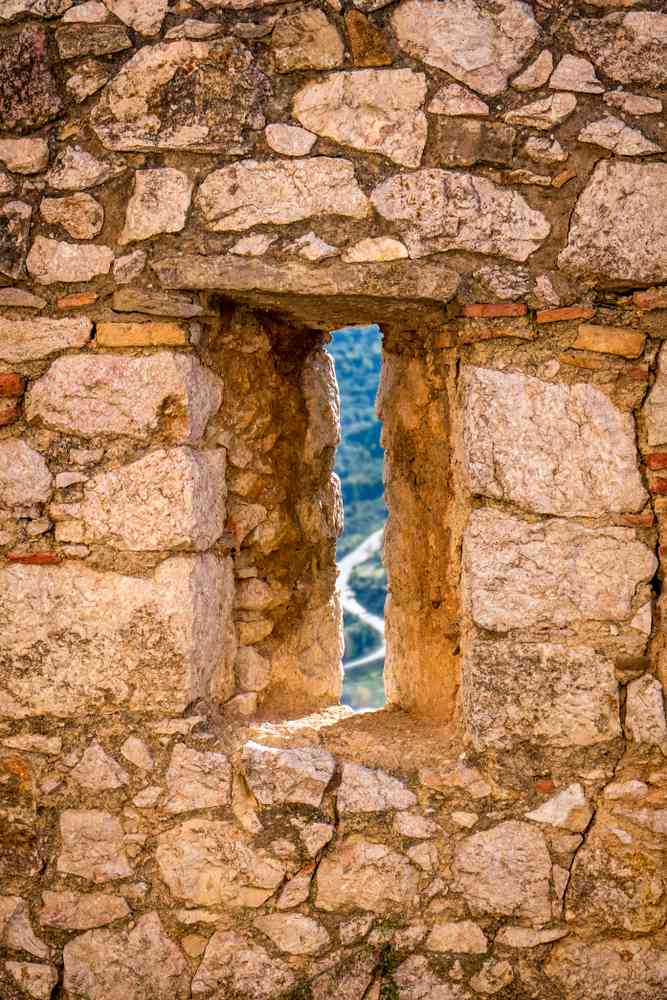 Mali prozor u zidu tvrđave, kroz koji se nazire krivudavi put.