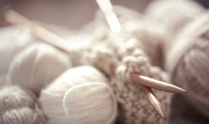 Klupko belo-bež vune. Započeto štrikanje i igle.