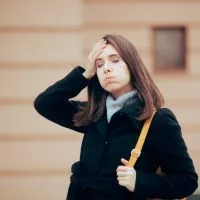 Žena na ulici se setila da je nešto zaboravila ili tako misli. Zatvorila je oči i stavila je ruku na glavu.