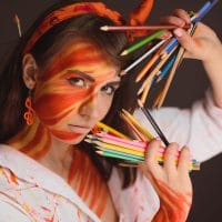 Žena umetnik, u rukama drži bojce, smišlja, boji lice.