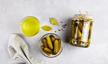 Tegla sa kiselim krastavcima, kiseli krastavci u činijici, lovorov list, a pored je čaša sa sokom od kiselih krastavaca.