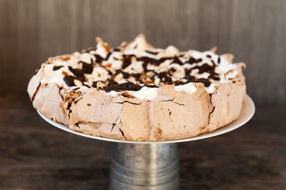 Pavlova torta odozgo ukrašena šlagom i topljenom čokoladom.