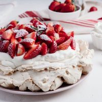 Mala Pavlova torta na stolu. Ukrašena jagodama i šlagom.