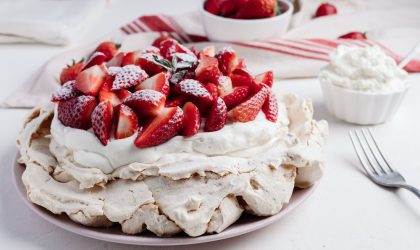 Mala Pavlova torta na stolu. Ukrašena jagodama i šlagom.