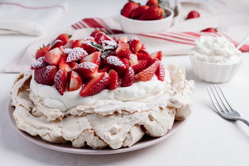 Mala Pavlova torta na stolu. Ukrašena jagodama i šlagom.